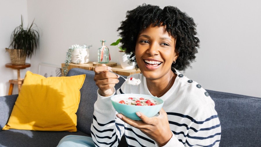 Portrait of happy young Latin American woman enjoying a healthy breakfast at home on the sofa 