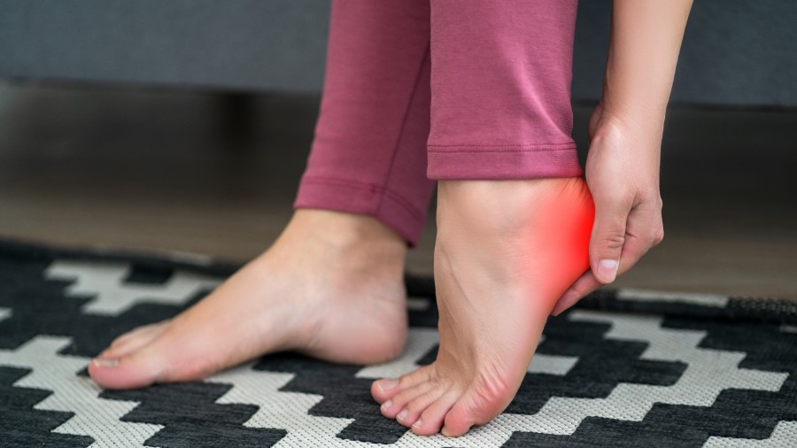 a close up of a woman's feet where she is holding her heel that is highlighted in red because of plantar fasciitis pain
